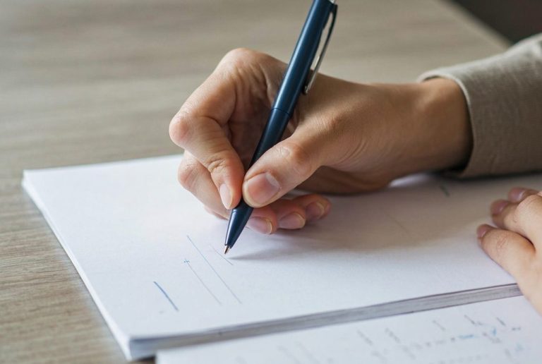 Eine Hand schreibt mit einem Stift auf einem leeren Blatt Papier.